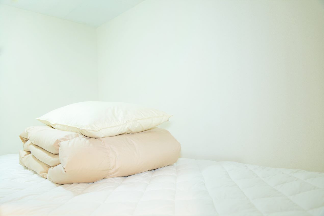 A neatly made bed with a white quilt and several beige pillows.