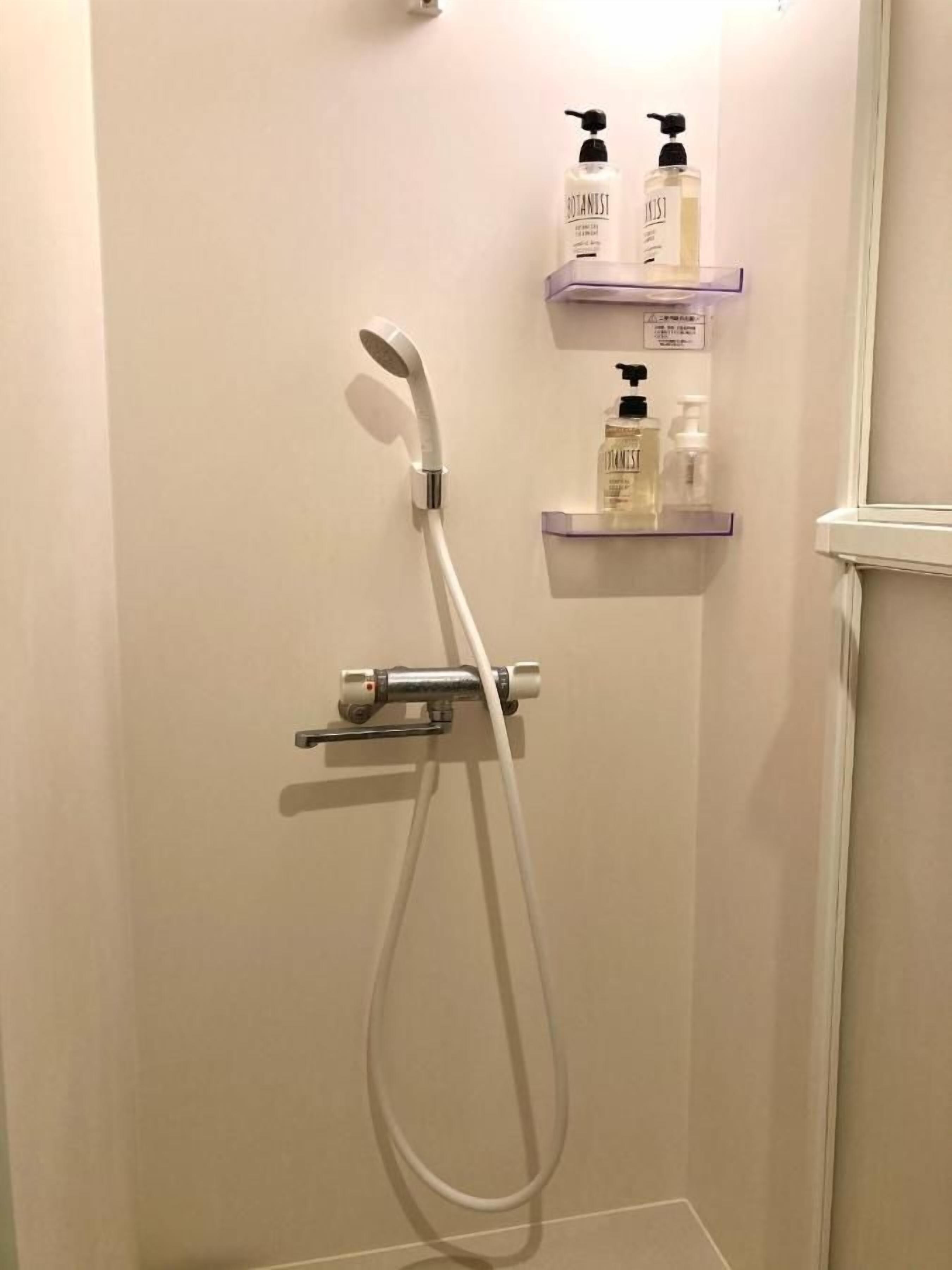 A shower with a handheld showerhead and a handheld shower attachment. There are two shelves with bottles of toiletries.