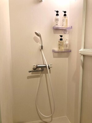 A shower with a handheld showerhead and a handheld shower attachment. There are two shelves with bottles of toiletries.