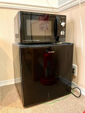A black refrigerator with a microwave on top, connected to a power outlet.