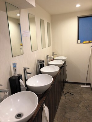 A bathroom with three sinks, a mirror, and a mop.
