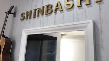 A wall with the name 'SHINBASHI' in large letters, a guitar leaning against the wall, and a doorway leading to another room.
