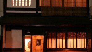 Perinteinen japanilainen rakennus, jossa on puinen ulkoverhous, laatoitettu sisäänkäynti ja penkki ulkona.