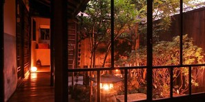Ein traditionelles japanisches Interieur mit Holzboden, einem Raum mit Tatami-Matten und Blick durch ein Fenster mit Holzgitter.