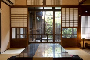 Ein traditioneller japanischer Raum mit Tatami-Bodenbelag, Schiebetüren und Blick auf einen Garten.