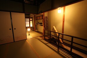 Un intérieur japonais traditionnel avec un sol recouvert de tatamis, des portes coulissantes et un escalier doté d’une rampe en bois.
