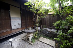Un jardin japonais traditionnel avec une lanterne en pierre, un petit étang et une clôture en bois.