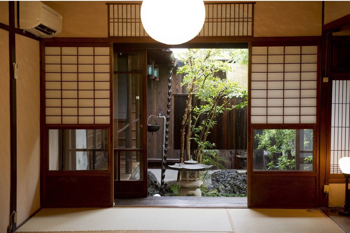 A traditional Japanese room with tatami flooring, sliding doors, and a view of a garden with a stone lantern.
