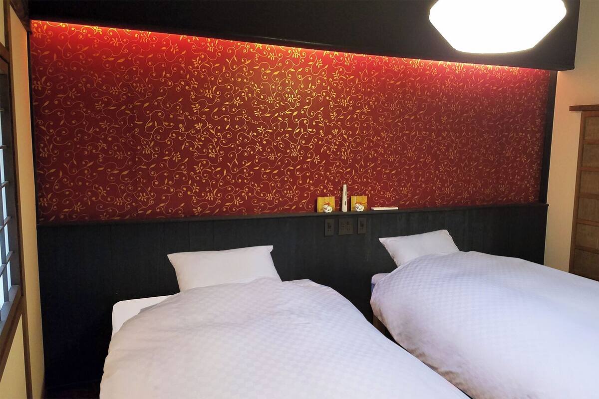 A hotel room with two beds, a red patterned wall, and a wooden wardrobe.