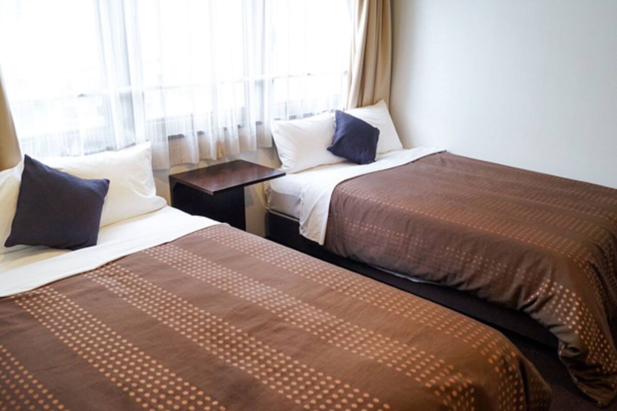 A hotel room with two beds, a nightstand, and a window with curtains.