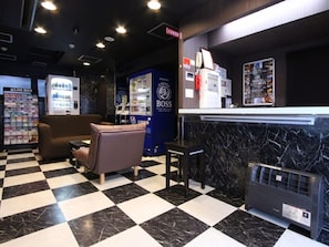 A checkered floor, a couch, a refrigerator, vending machines, and a wall with a poster. - Hotel Livemax Budget Umeda (Osaka)