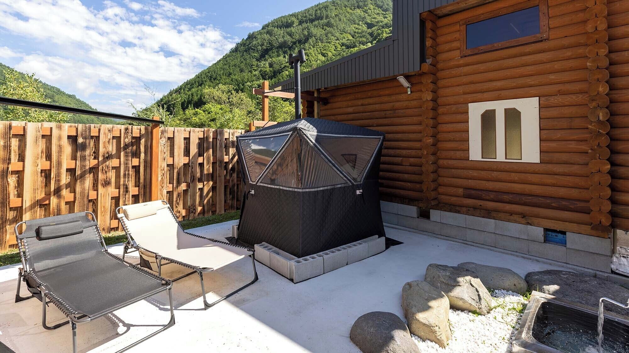 Una cabaña de madera con un patio, mobiliario exterior, una parrilla y una pequeña fuente de agua.