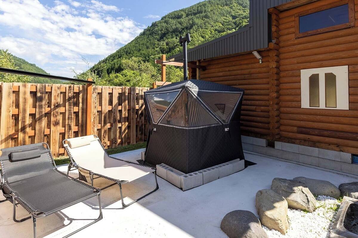 A wooden cabin with a patio, outdoor seating, a grill, and a small water feature.