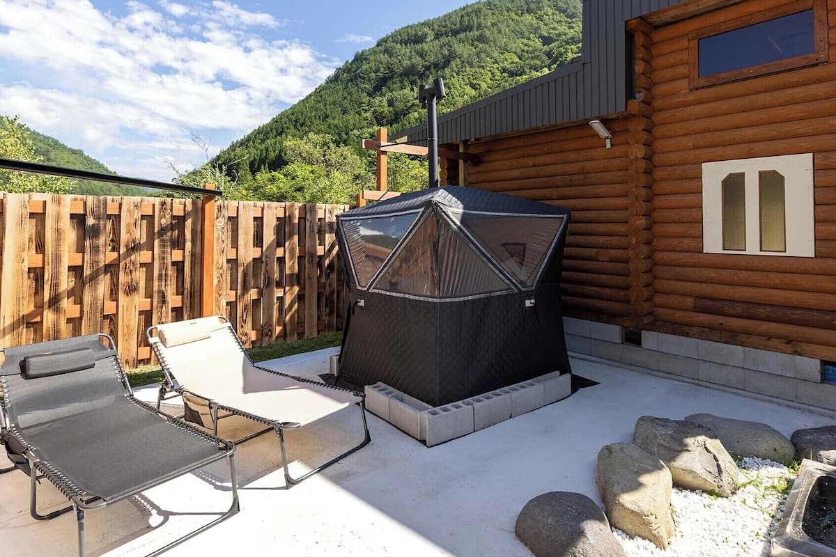 Una cabaña de madera con un patio, mobiliario exterior, una parrilla y una pequeña fuente de agua.