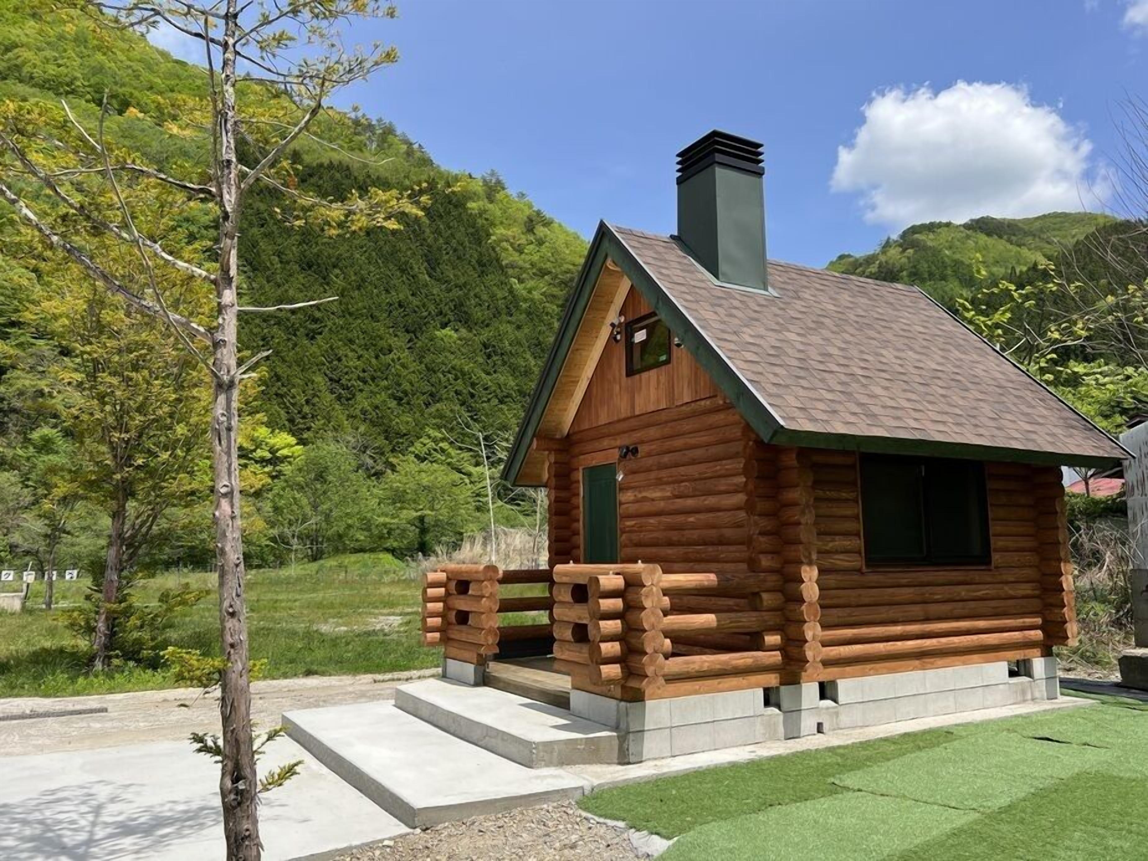 Una cabaña de troncos con chimenea, puerta verde y porche de madera.