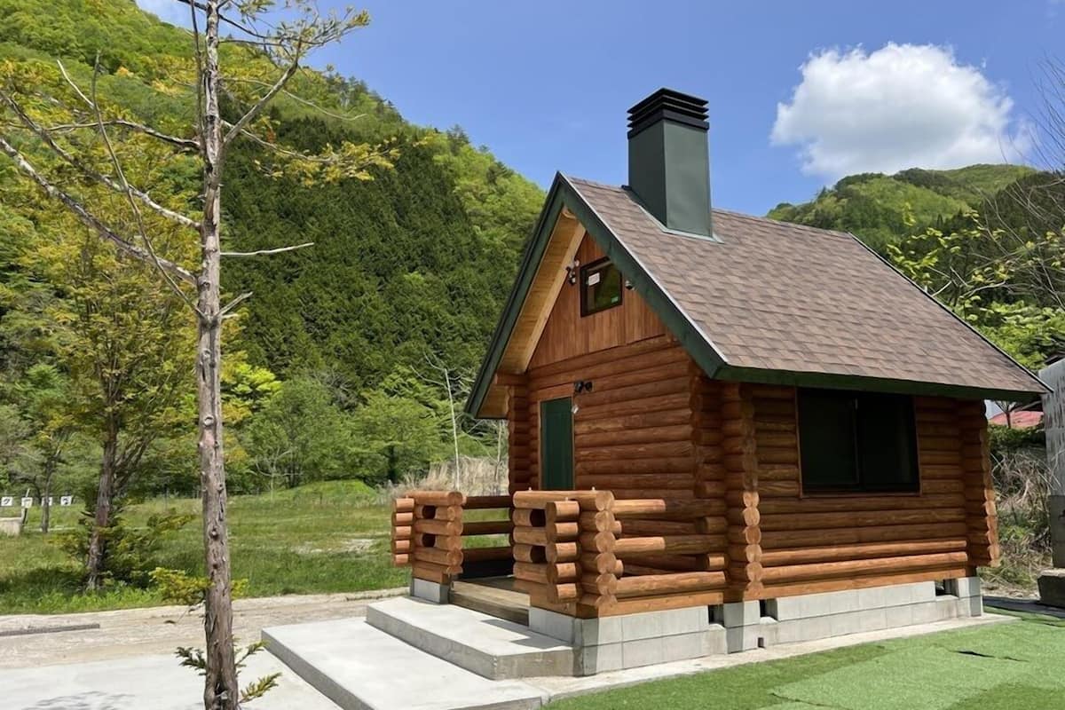 A log cabin with a chimney, a green door, and a wooden porch.