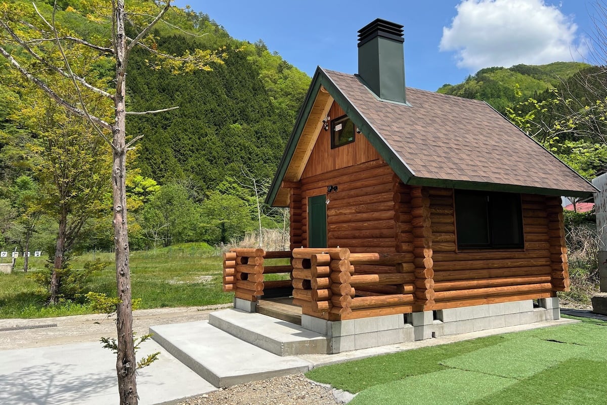 A log cabin with a pitched roof, a chimney, and a small porch with wooden railings.