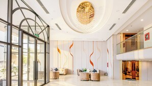 A spacious lobby with a glass entrance, modern furniture, and a decorative ceiling. - GRAND LUX by BRIO (Da Nang)