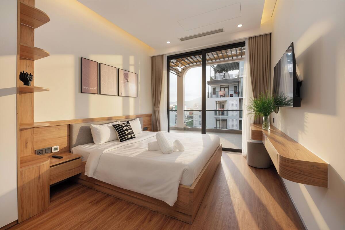 Un dormitorio moderno con cama de madera, mesitas de noche, televisor y vistas al balcón.