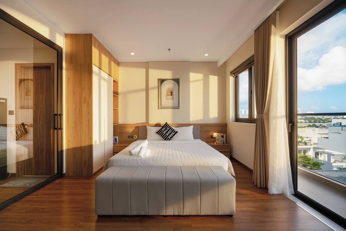 Una habitación de hotel moderna con una cama grande, un armario de madera, vistas de la ciudad y un ventanal amplio.