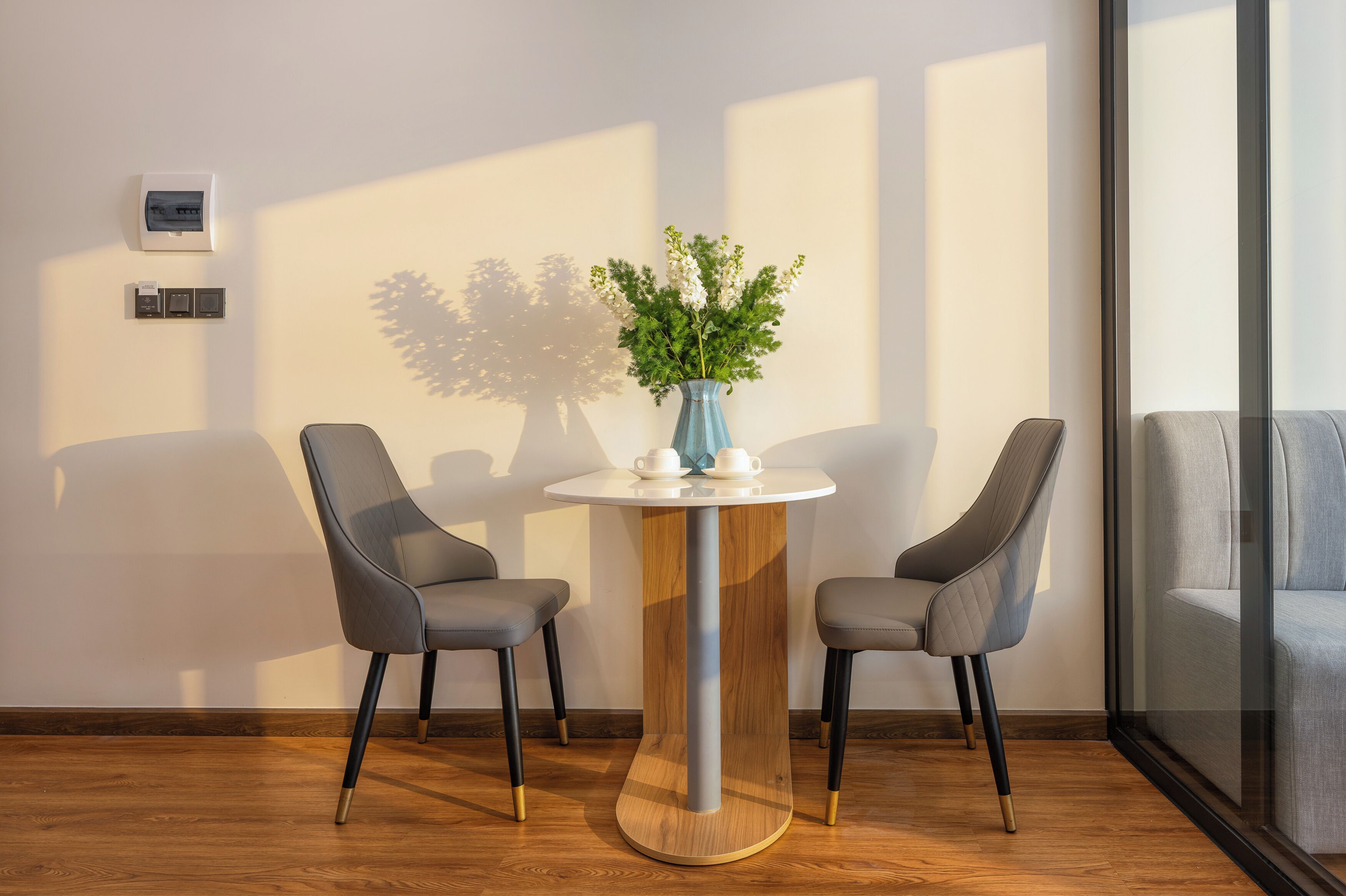 A modern room with a round table, two chairs, a vase with flowers, and a thermostat on the wall.