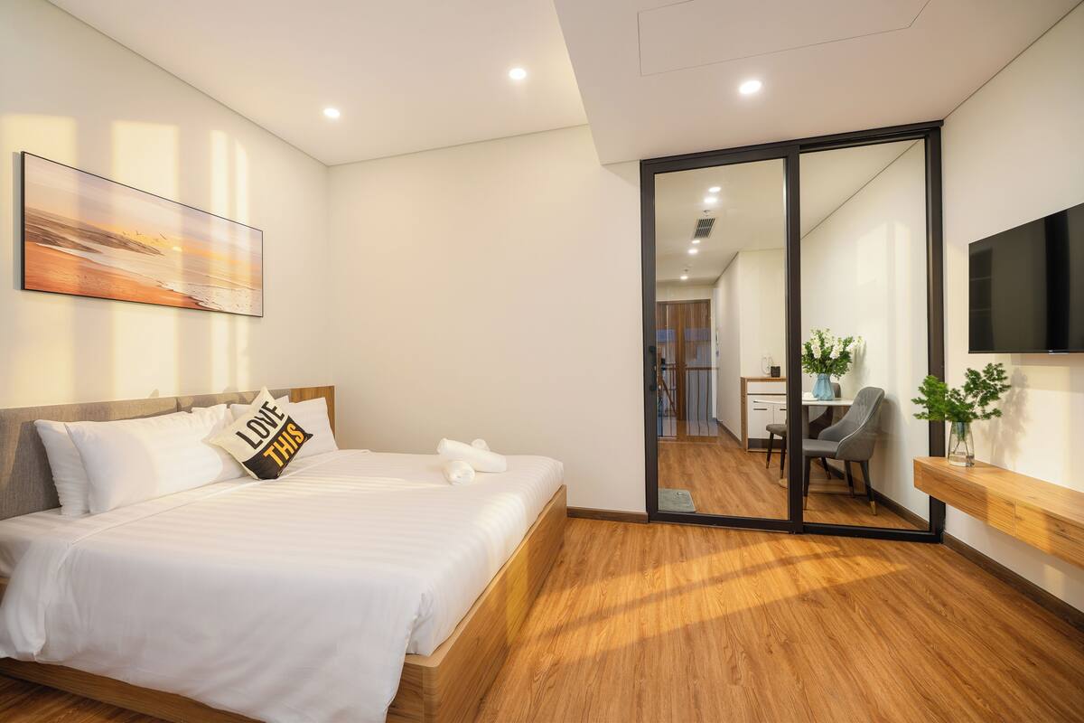 Una habitación de hotel moderna con una cama, un espejo grande, un televisor de pantalla plana y piso de madera.