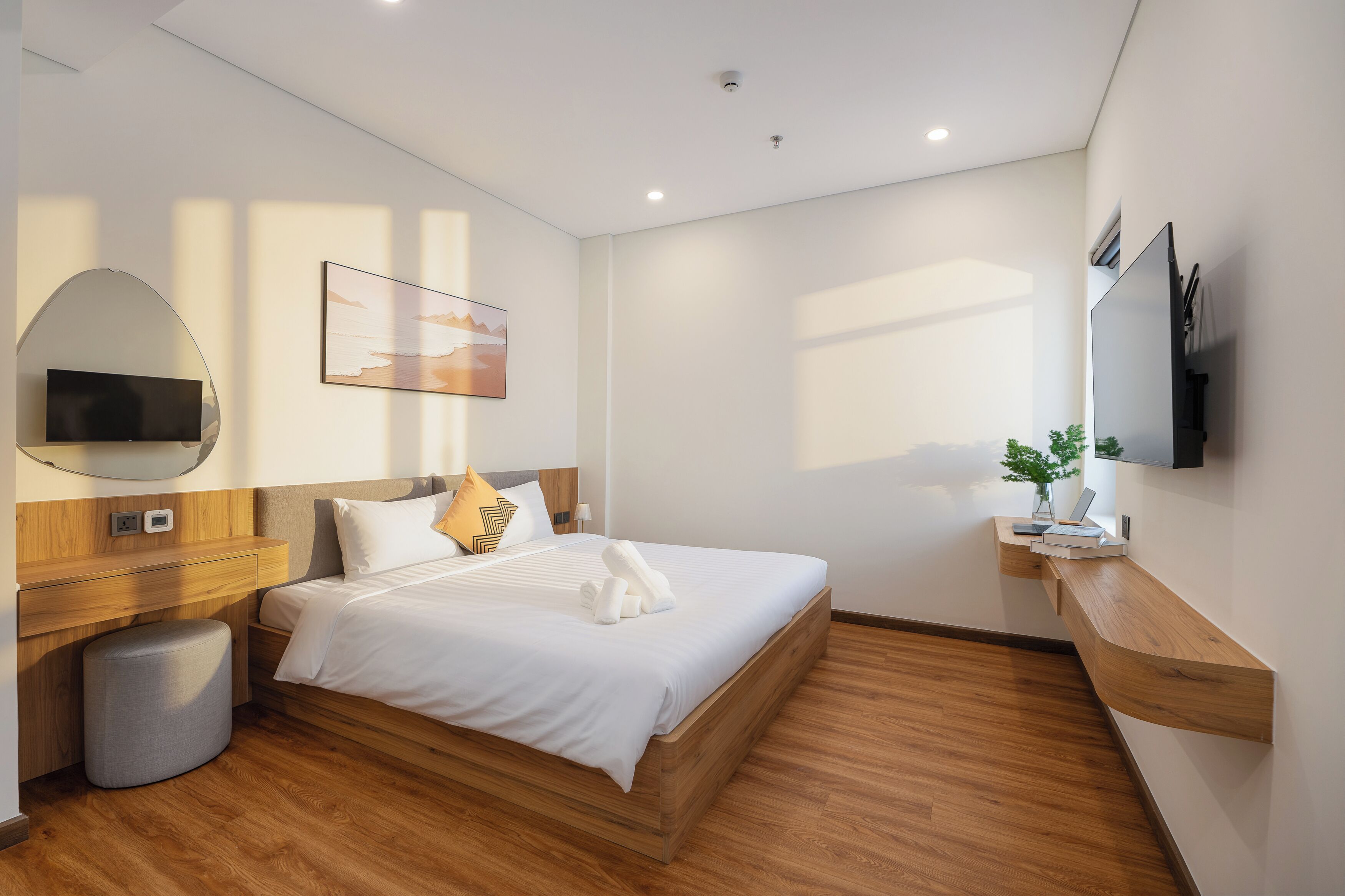 A modern hotel room with a wooden bed, a flat-screen TV, a bedside table, and a wall-mounted TV.