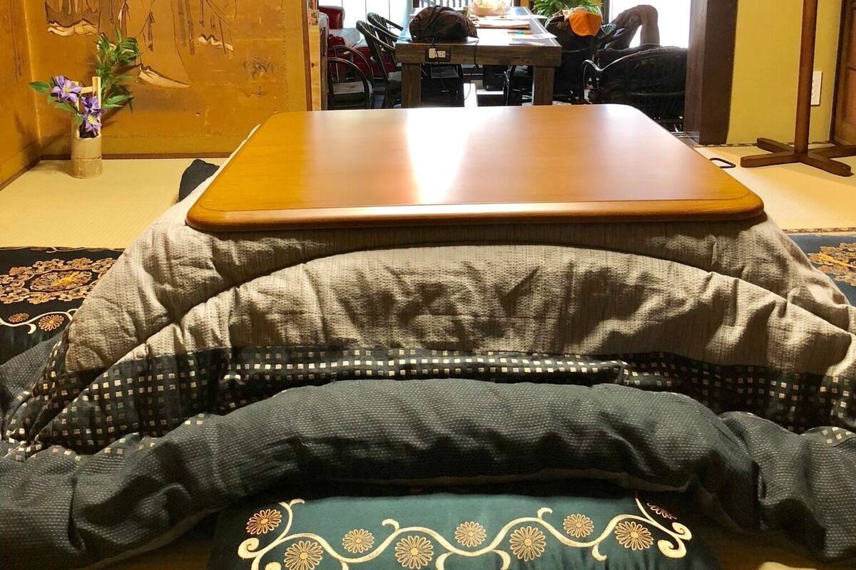 Um quarto japonês tradicional com tatames, uma mesa baixa, almofadas e um candeeiro pendente.