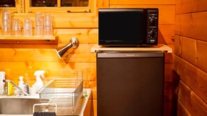 Eine kompakte Küche mit einer schwarzen Panasonic-Mikrowelle auf einem Kühlschrank, einem Spülbecken mit Geschirrständern und Holzwänden.