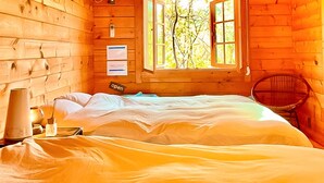 A wooden cabin room with a bed, a chair, and a window with a view of trees. - Asobi No Cottage Hatsukaichi (Hatsukaichi)