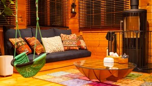 A cozy living room with a sofa, colorful cushions, a hanging chair, a glass coffee table, and a wood-burning stove. - Asobi No Cottage Hatsukaichi (Hatsukaichi)