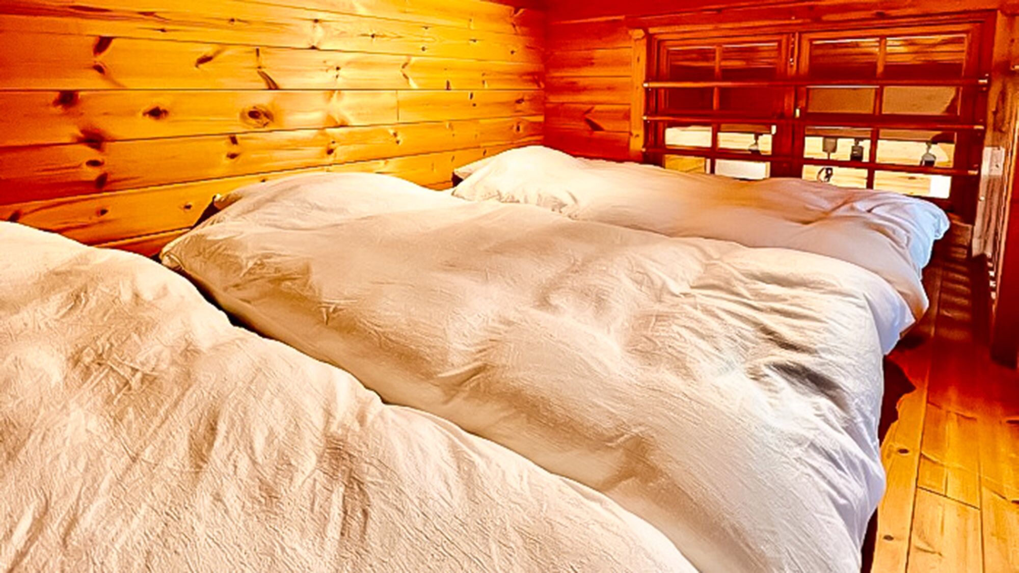 Een blokhut met houten wanden, een bed met wit beddengoed en een raam met uitzicht.