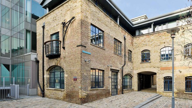 A historic building with a brick facade, large windows, and a modern glass structure adjacent to it.