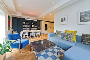 A modern living room with a blue sofa, a coffee table, and a bookshelf. - Elegant 2 bedroom flat - King's Cross (Greater London)