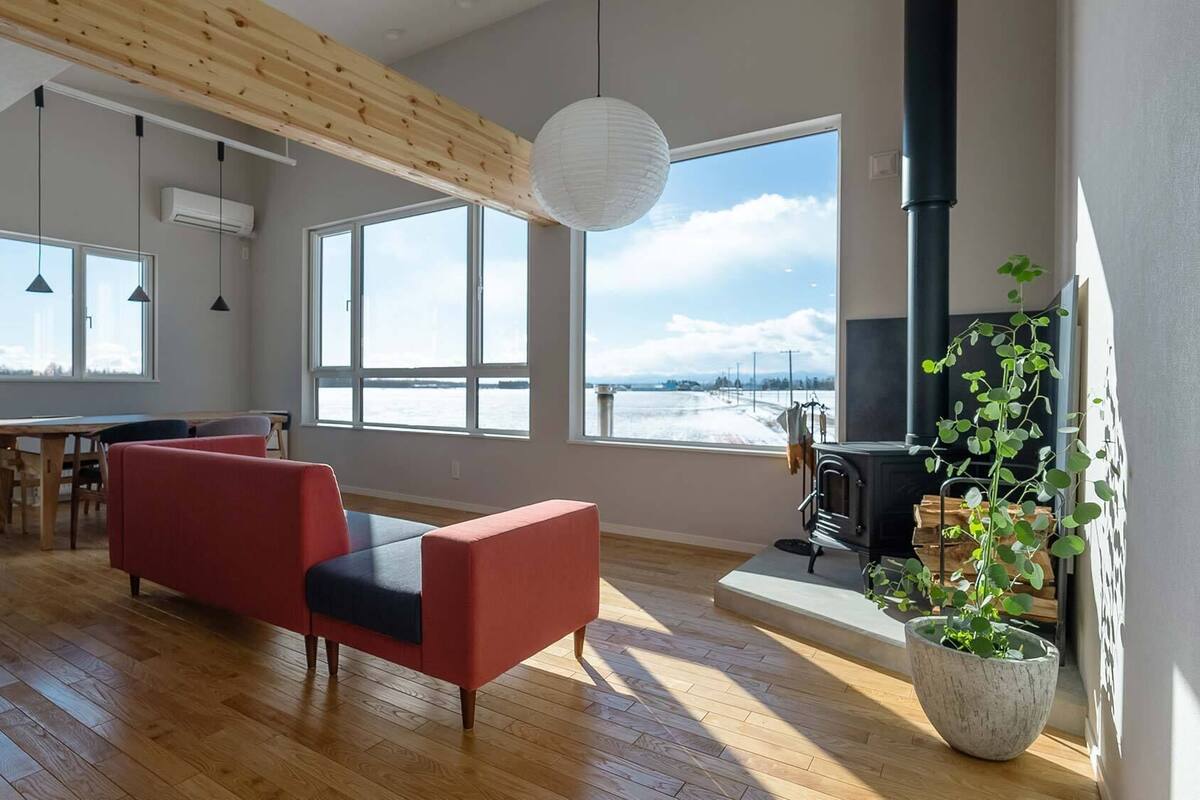A modern living room with a fireplace, large windows, and a view of a snowy landscape.