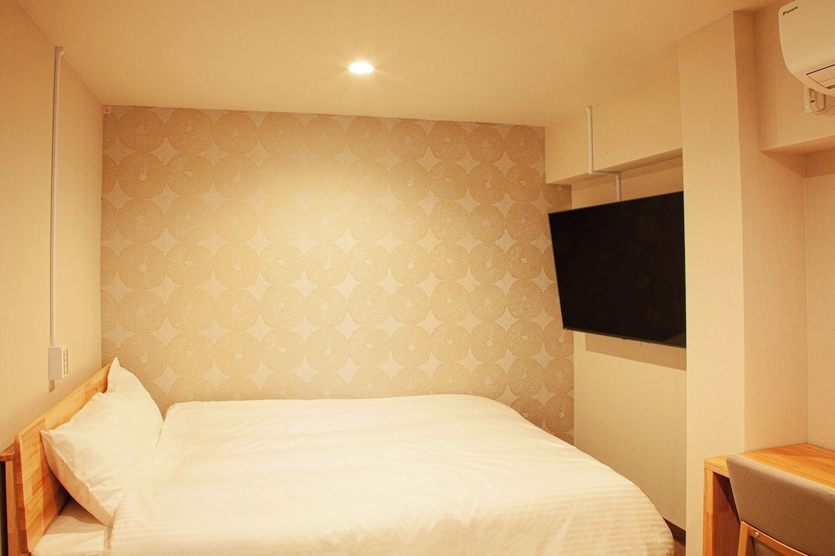 A hotel room with a bed, a television mounted on the wall, and a desk.