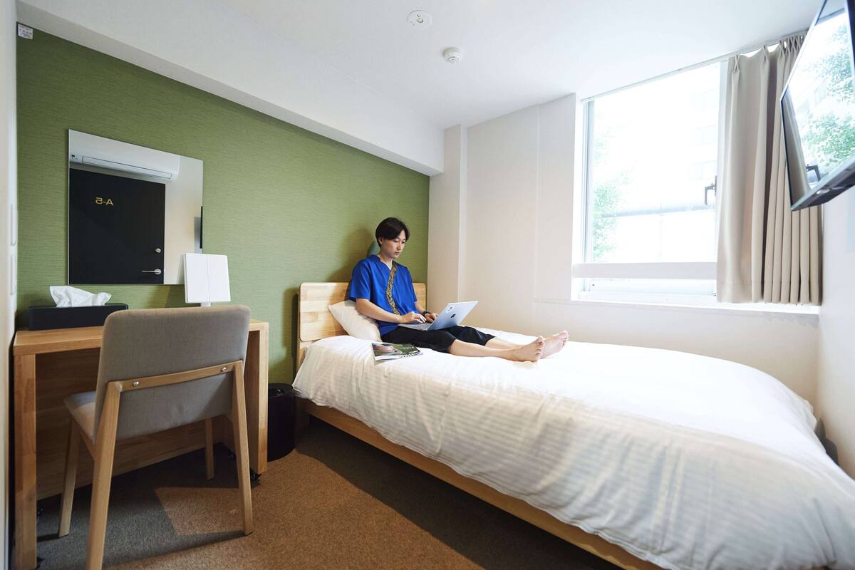 A hotel room with a bed, a desk, a chair, a mirror, and a window.