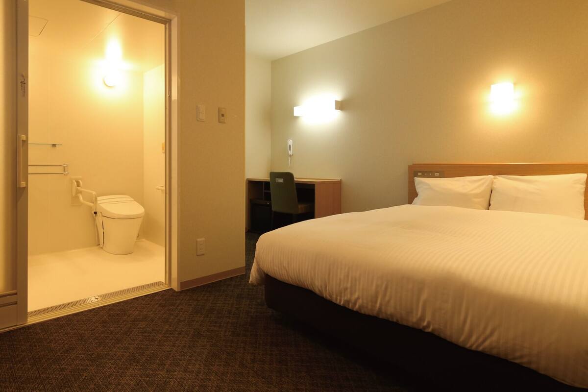 A hotel room with a bed, a desk, and a toilet.