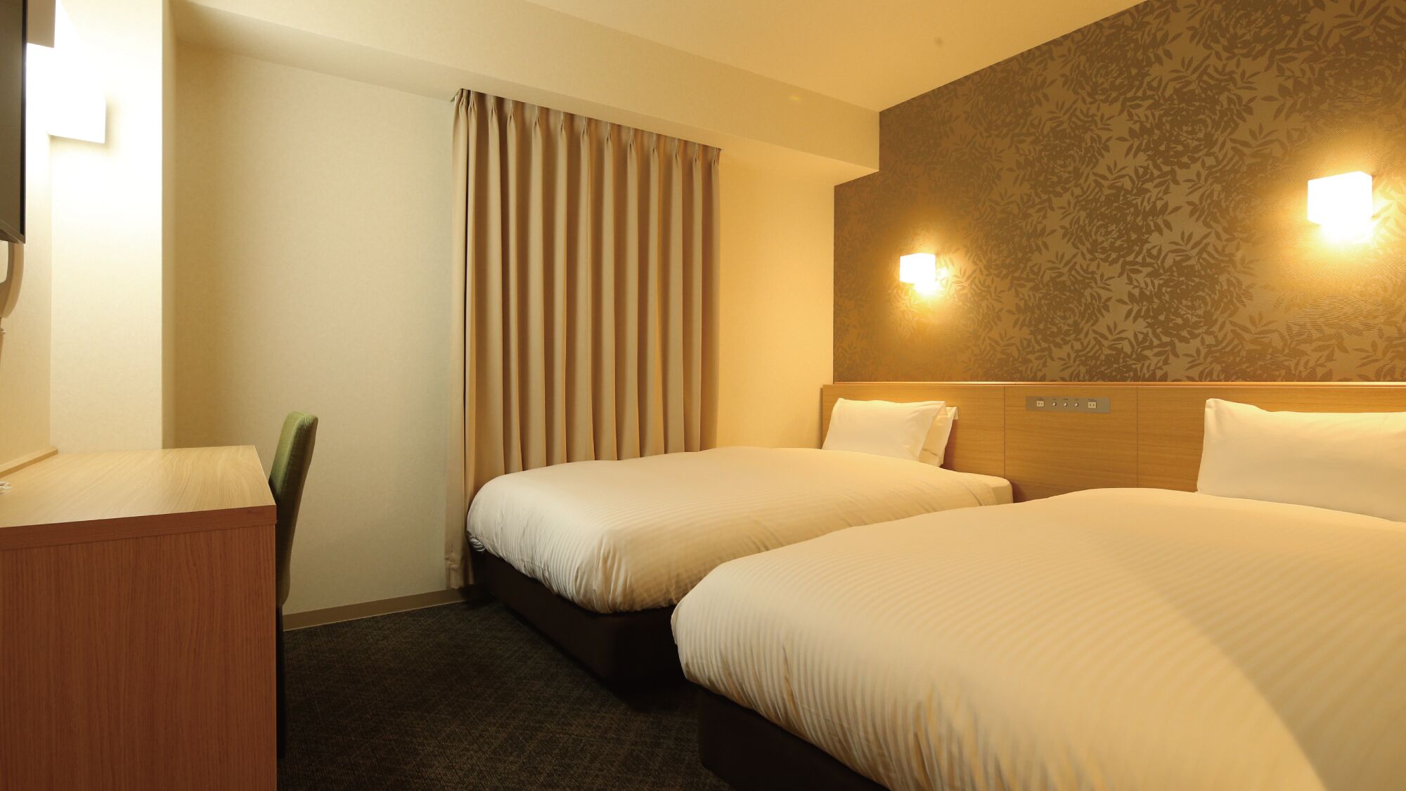 Ein Hotelzimmer mit zwei Betten, einem Schreibtisch, einem Stuhl und einer Wandlampe.