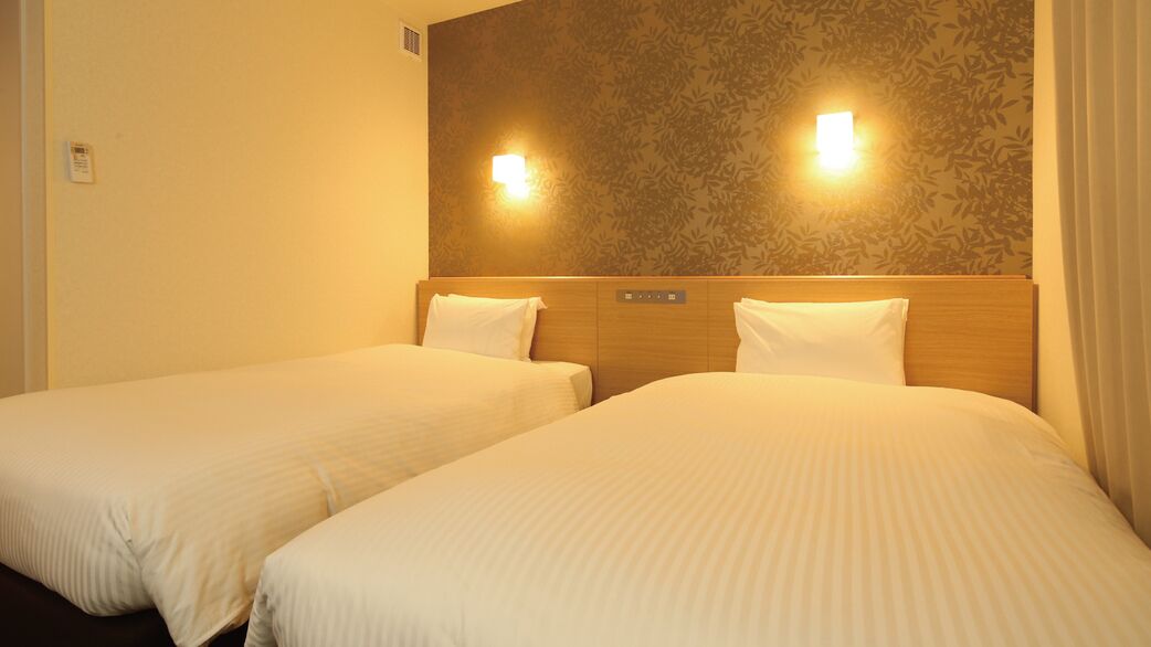 A hotel room with two beds, a wooden headboard, and wall-mounted lights.