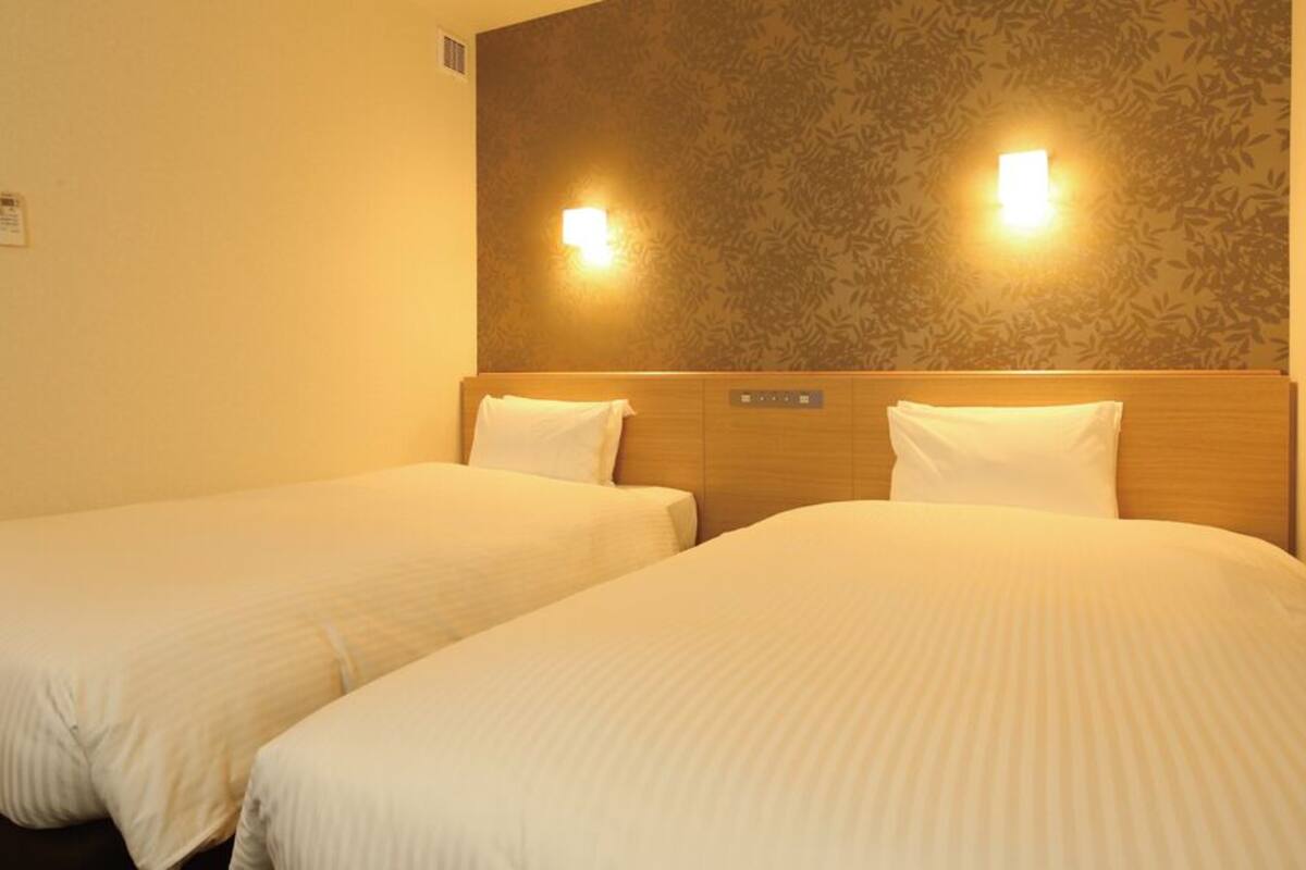 A hotel room with two beds, a wooden headboard, and wall-mounted lights.