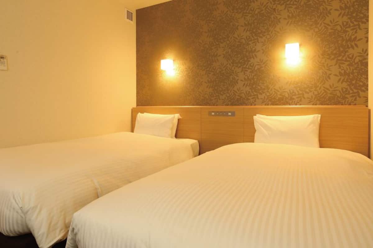 A hotel room with two beds, a wooden headboard, and wall-mounted lights.