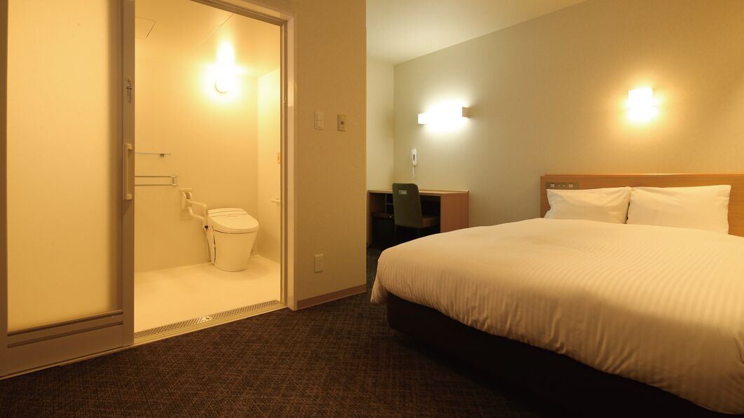 A hotel room with a bed, a desk, a chair, and a toilet.