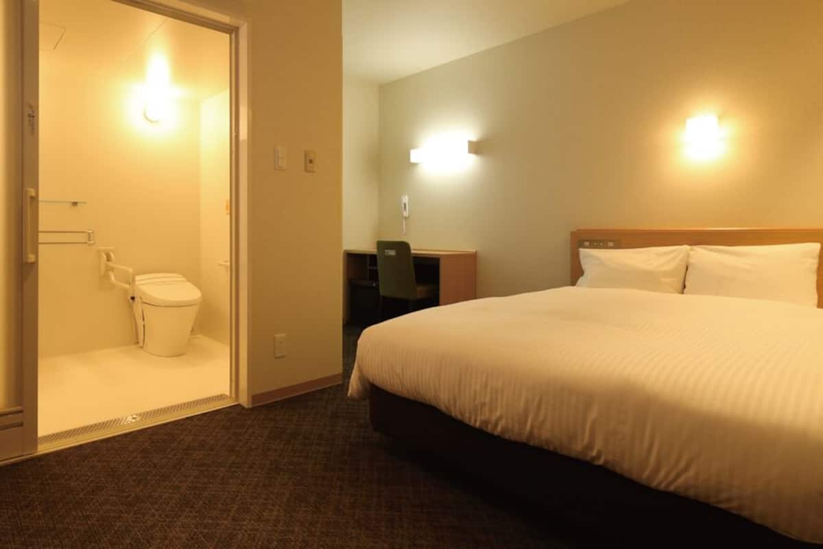 A hotel room with a bed, a desk, a chair, and a toilet.