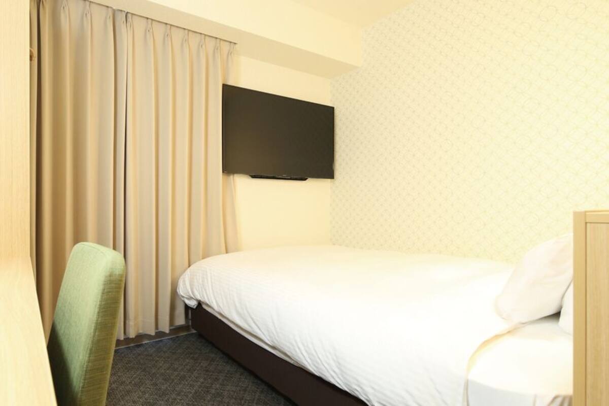 A hotel room with a bed, a chair, a flat-screen TV, and a curtain.