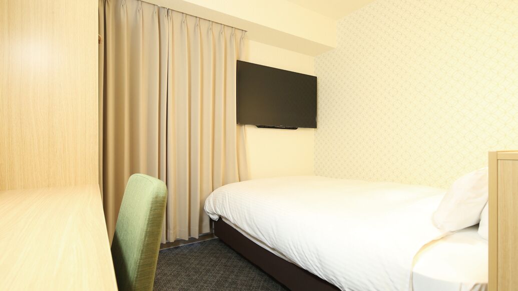 A hotel room with a bed, a chair, a flat-screen TV, and a curtain.