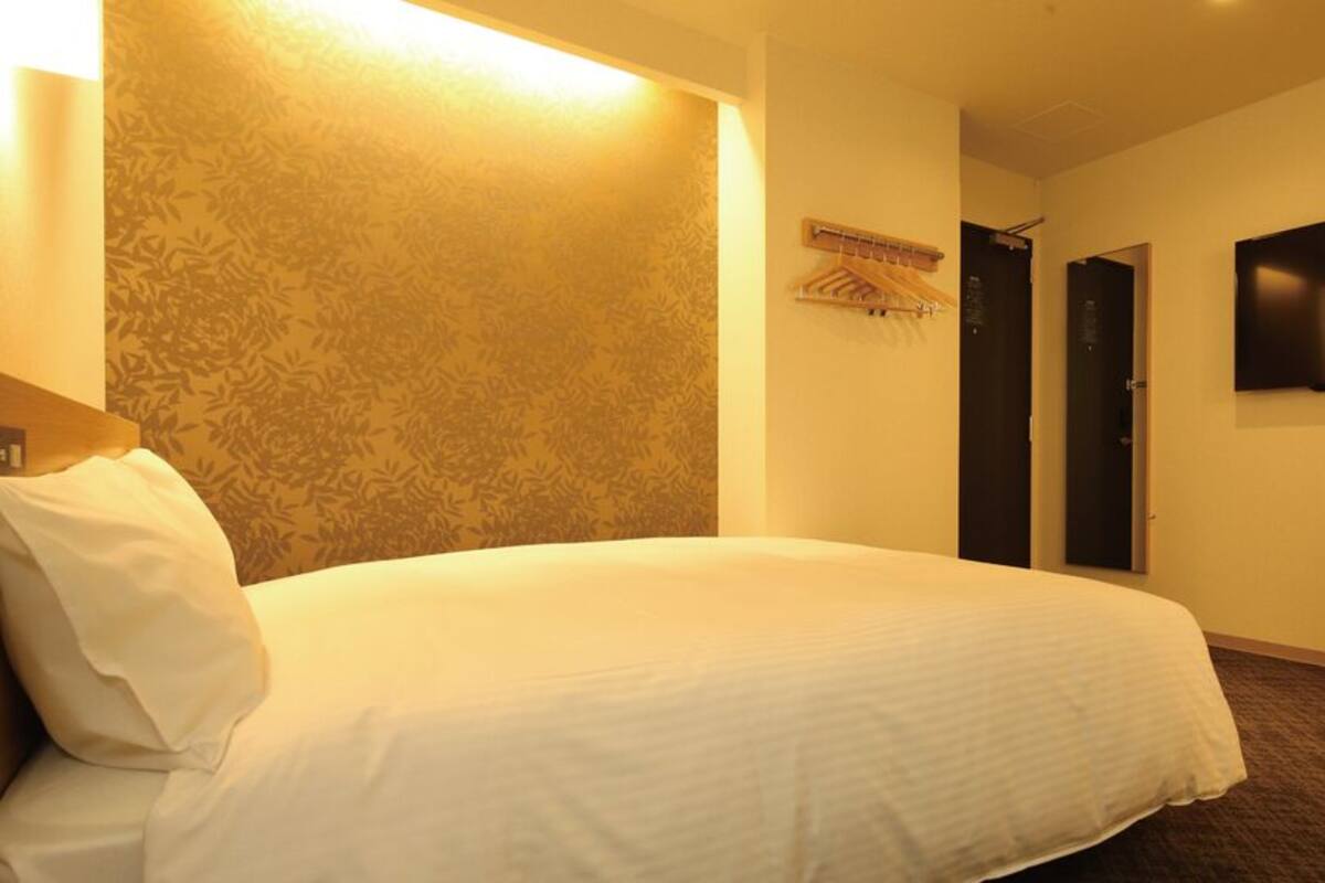 A hotel room with a bed, a wall-mounted TV, and a door.