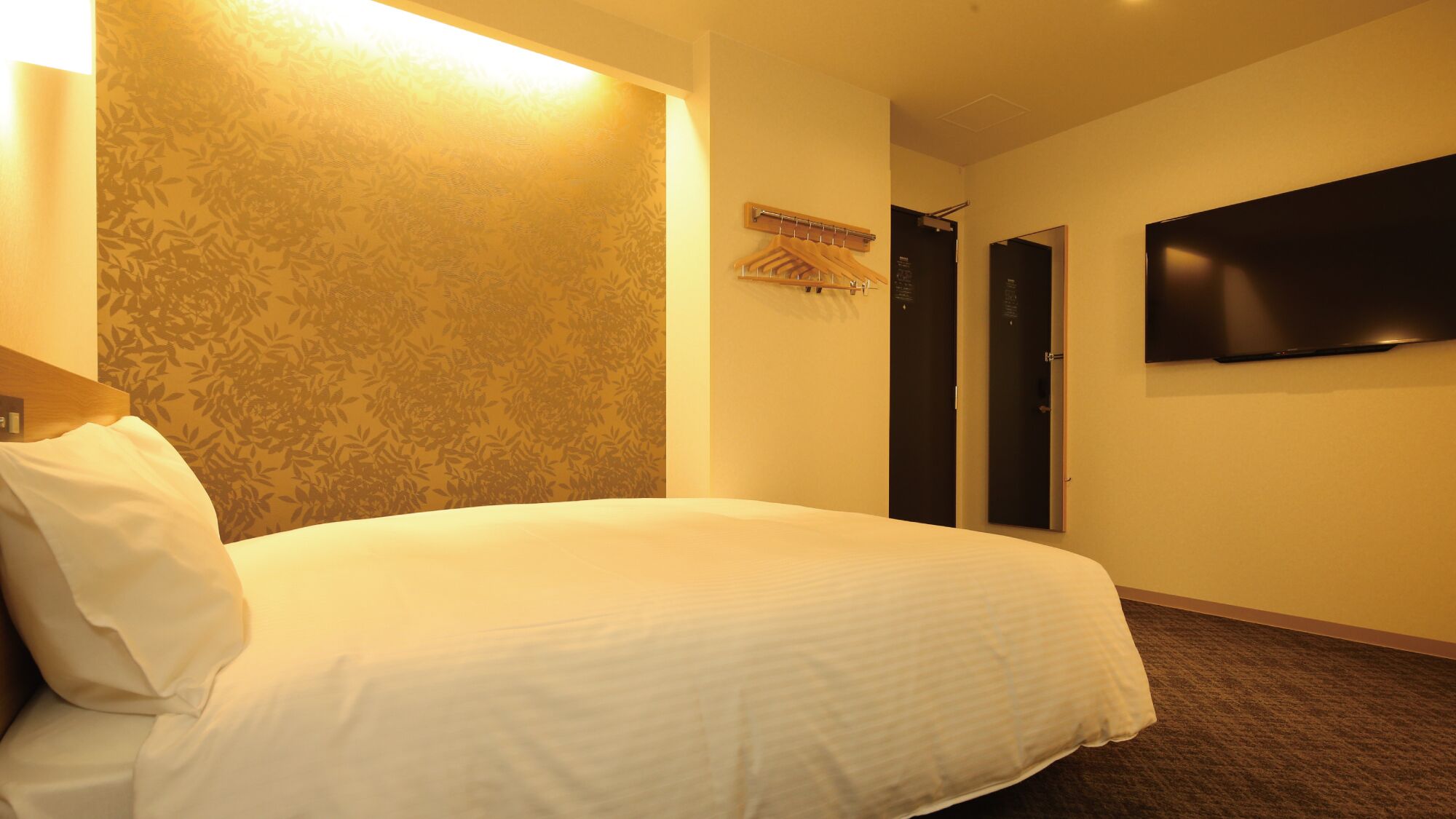 Ein Hotelzimmer mit Bett, einem an der Wand befestigten Fernseher und einer Tür mit Kleiderhaken.