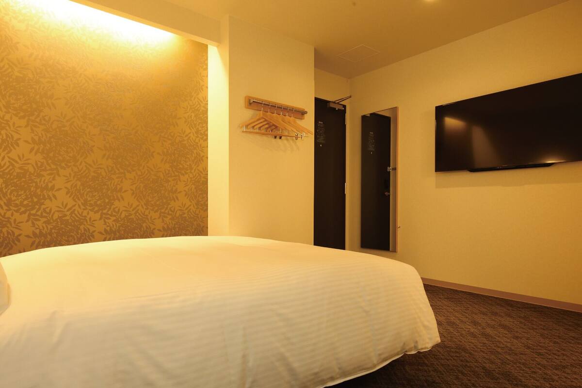 A hotel room with a bed, a wall-mounted TV, and a door with a coat rack.