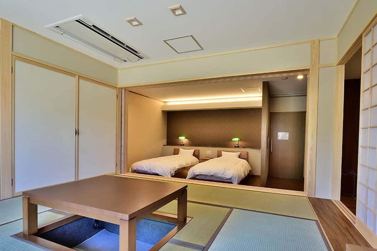 A traditional Japanese-style room with tatami flooring, a low wooden table, two beds with pillows, and a sliding door.